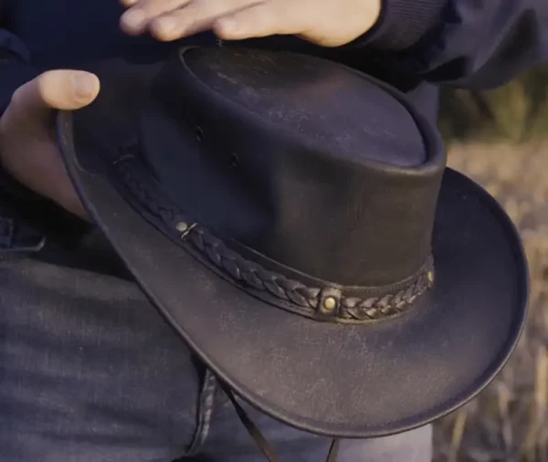 man holding a black leather hat by wombat