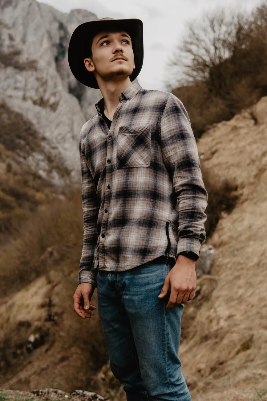 Man wearing a leather hat and checked shirt among rocky hills