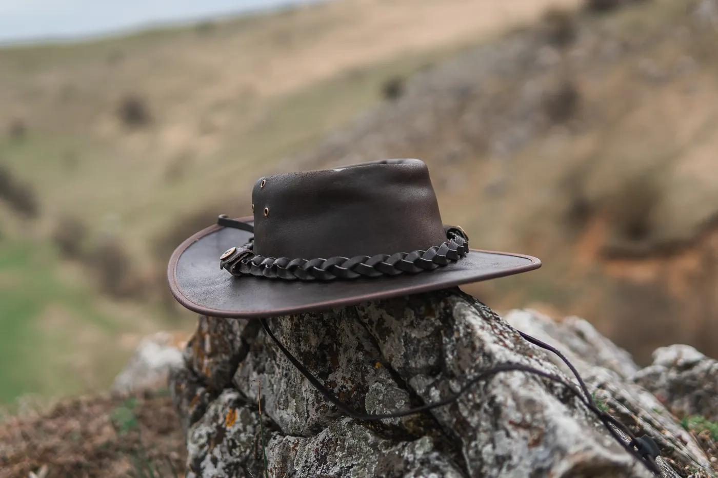 Dark leather hat with a braided band resting on a rock in the countryside